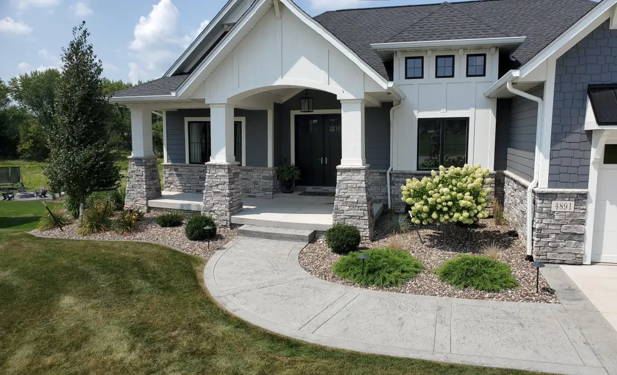 Curved stamped walkway with stone veneer columns and hydrangeas