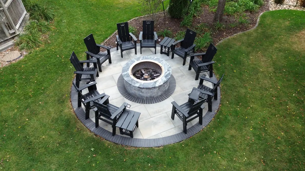 Circle of Adirondack chairs around paver fire pit on manicured lawn